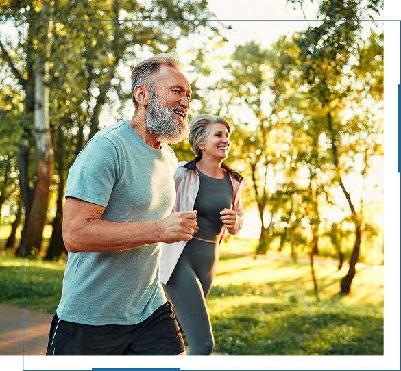 An elderly couple jogging together outdoors in a sunny park.
